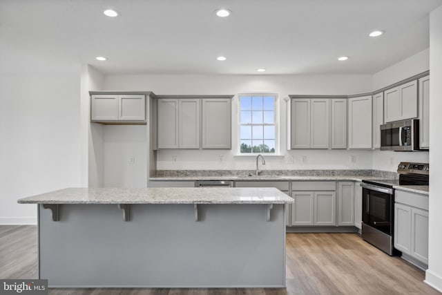 kitchen featuring gray cabinetry, a breakfast bar, light wood-type flooring, stainless steel appliances, and a sink