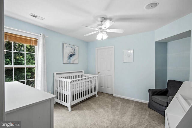 bedroom featuring visible vents, light carpet, a nursery area, baseboards, and ceiling fan