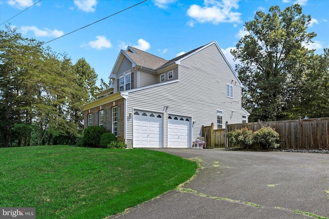 view of side of property featuring aphalt driveway, a lawn, a garage, and fence