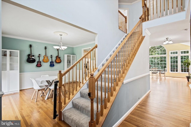 staircase with ornamental molding, wood finished floors, an inviting chandelier, baseboards, and a towering ceiling