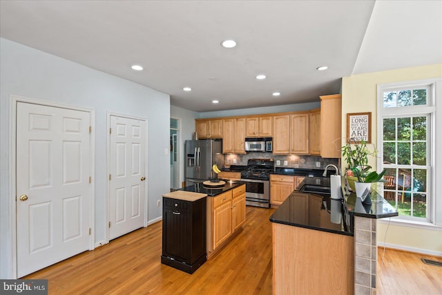 kitchen with dark countertops, backsplash, a center island, stainless steel appliances, and a sink