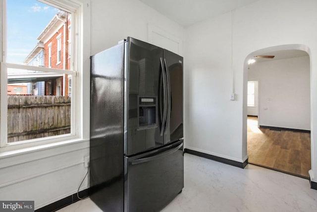 kitchen featuring black fridge with ice dispenser, arched walkways, white cabinets, baseboards, and ceiling fan