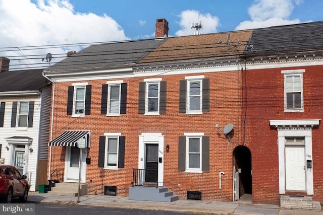 view of property featuring brick siding, entry steps, a chimney, and a shingled roof