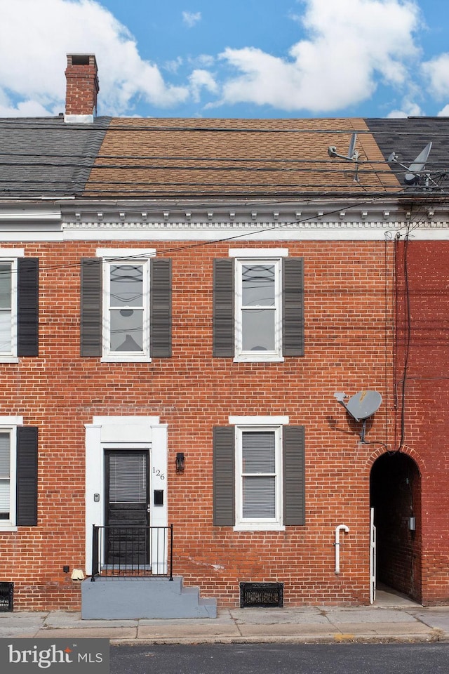 view of front of house featuring a shingled roof, brick siding, and a chimney