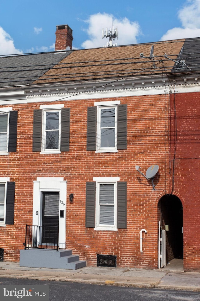 view of front of home with brick siding, roof with shingles, and a chimney