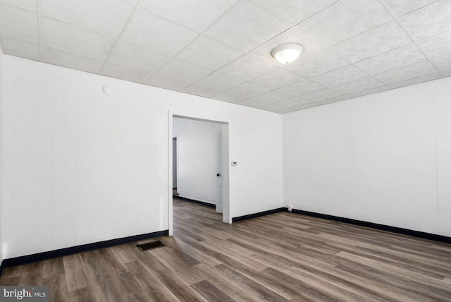 spare room featuring visible vents, a paneled ceiling, baseboards, and wood finished floors