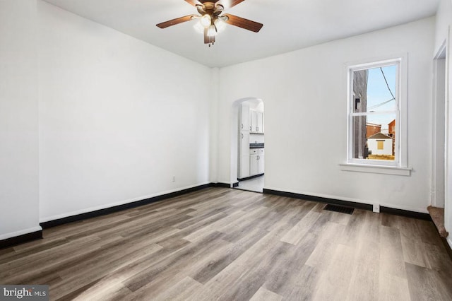 unfurnished room featuring a ceiling fan, wood finished floors, visible vents, baseboards, and arched walkways