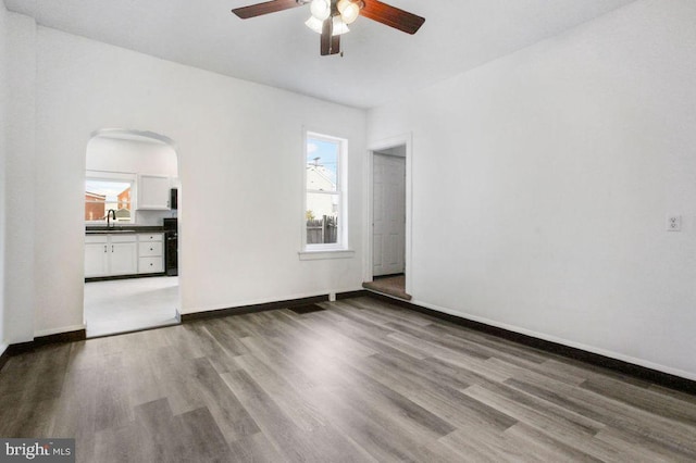 spare room featuring baseboards, wood finished floors, arched walkways, a ceiling fan, and a sink