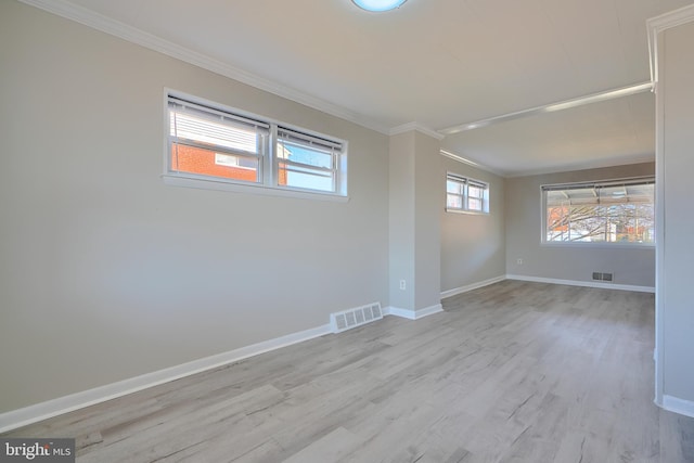 empty room with visible vents, light wood-style flooring, baseboards, and ornamental molding