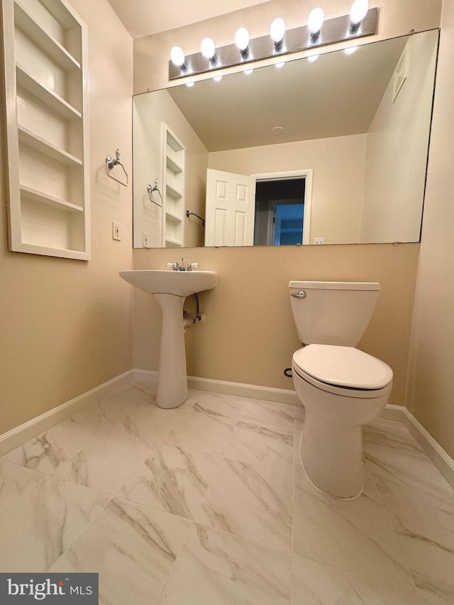 bathroom featuring marble finish floor, built in shelves, toilet, and baseboards