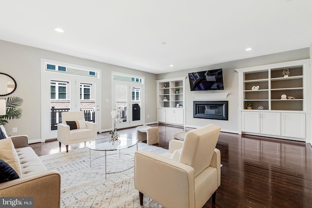 living area featuring built in shelves, baseboards, hardwood / wood-style floors, recessed lighting, and a glass covered fireplace