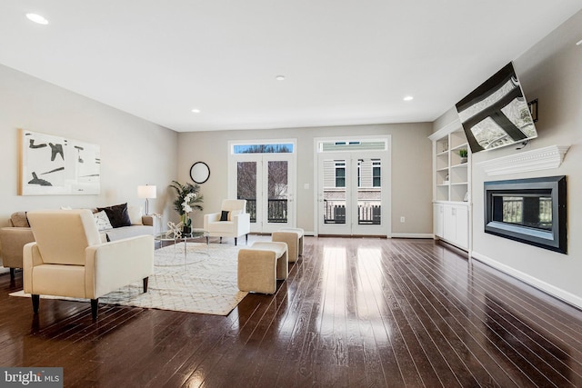 living area featuring built in features, a glass covered fireplace, dark wood-style floors, recessed lighting, and baseboards