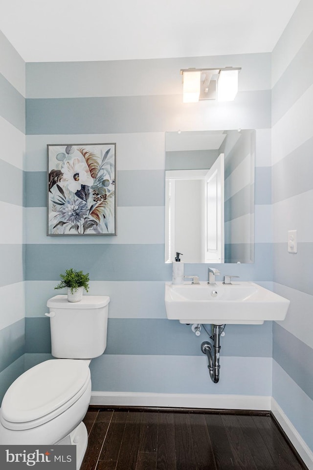 half bathroom with baseboards, toilet, and wood finished floors