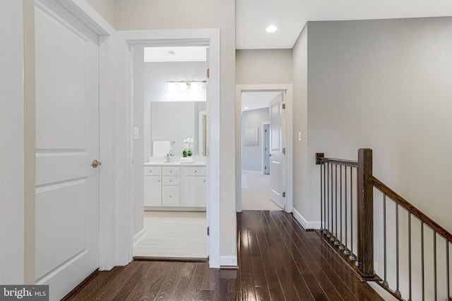 corridor with an upstairs landing, wood finished floors, and baseboards