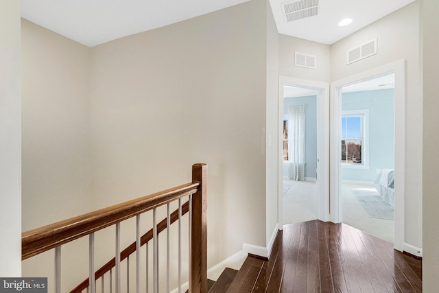 corridor with an upstairs landing, visible vents, and dark wood-style flooring