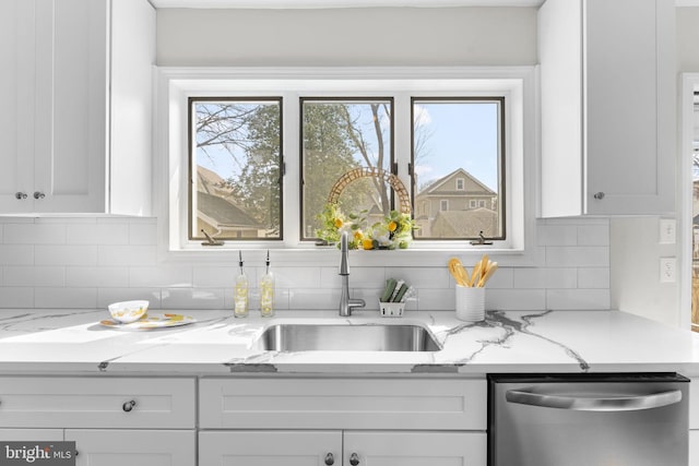 kitchen with stainless steel dishwasher, white cabinets, light stone countertops, and backsplash