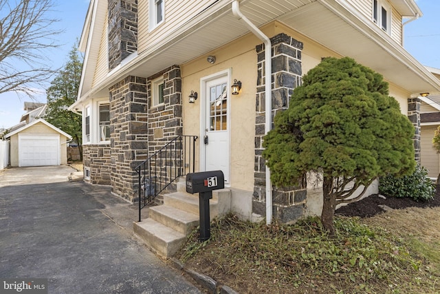 property entrance with aphalt driveway, stone siding, and a detached garage