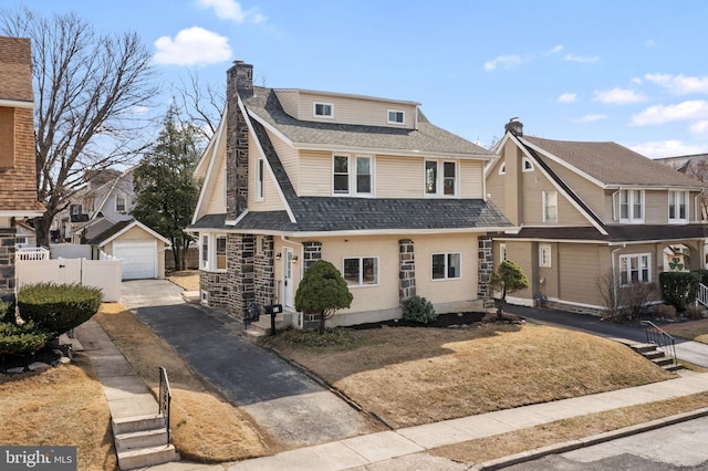 view of front facade with fence, roof with shingles, an outdoor structure, a garage, and a chimney