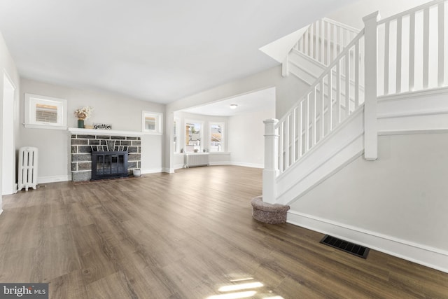 unfurnished living room featuring stairway, wood finished floors, visible vents, radiator heating unit, and a fireplace