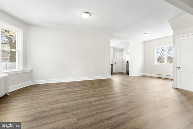 unfurnished living room featuring baseboard heating, baseboards, and wood finished floors