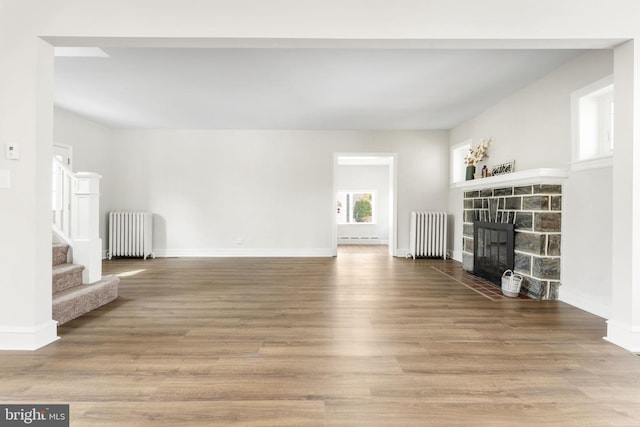 unfurnished living room featuring a stone fireplace, stairs, radiator heating unit, and wood finished floors