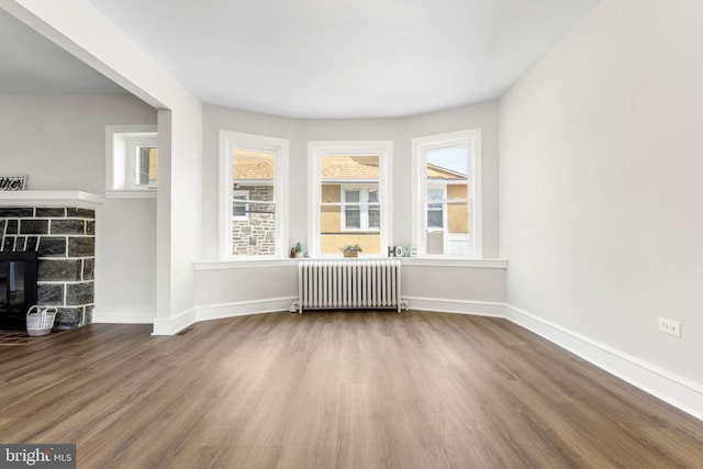 unfurnished living room featuring radiator, a fireplace, baseboards, and wood finished floors