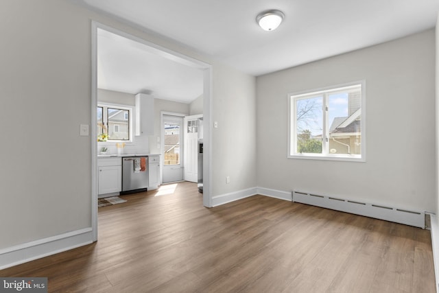 unfurnished living room with a baseboard radiator, baseboards, a healthy amount of sunlight, and wood finished floors