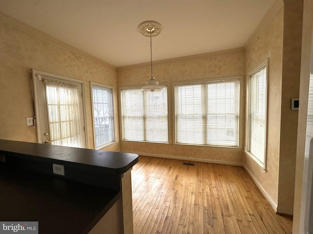 unfurnished dining area with visible vents, light wood-style flooring, baseboards, and ornamental molding