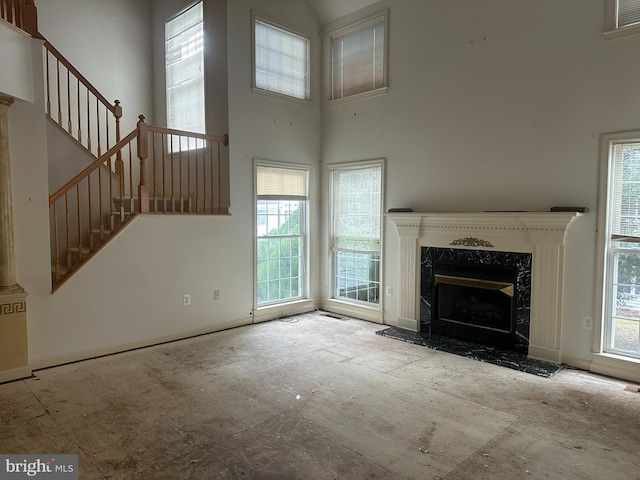 unfurnished living room featuring a wealth of natural light, stairway, a towering ceiling, and a high end fireplace