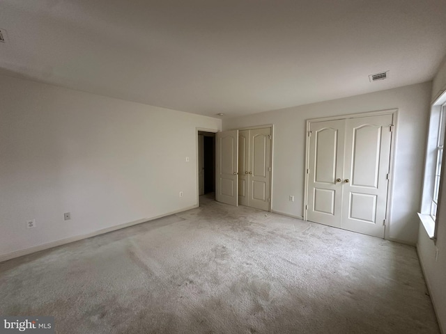 unfurnished bedroom with baseboards, visible vents, multiple closets, and light carpet