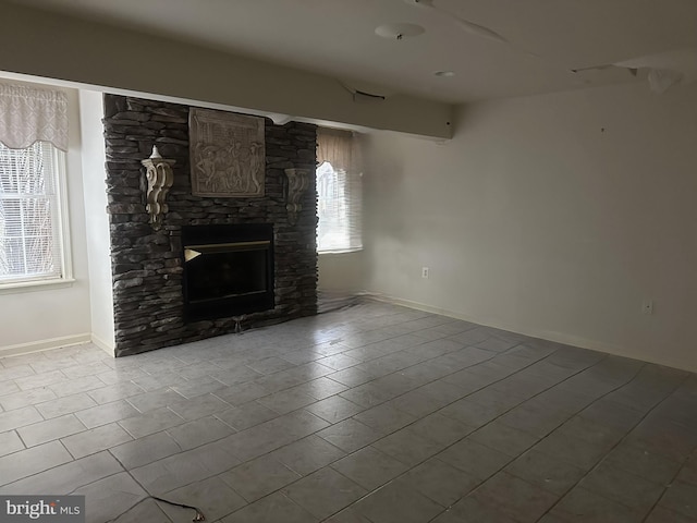 unfurnished living room featuring a stone fireplace, baseboards, and a wealth of natural light