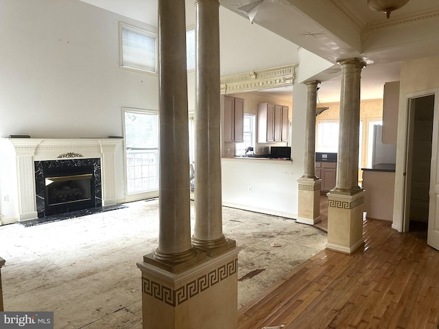 unfurnished living room featuring a fireplace, a high ceiling, wood finished floors, and ornate columns