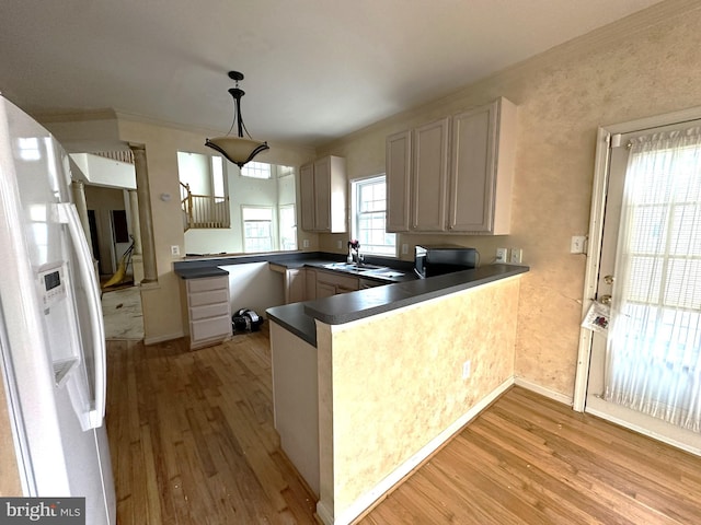 kitchen with a sink, dark countertops, light wood-style floors, white fridge with ice dispenser, and a peninsula