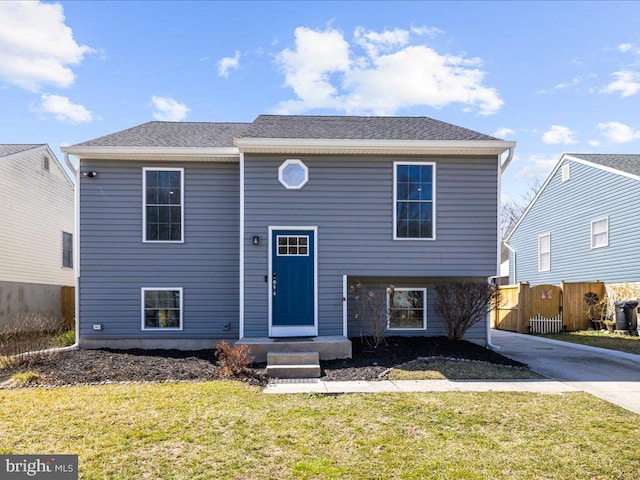 raised ranch featuring a front lawn, fence, and a shingled roof