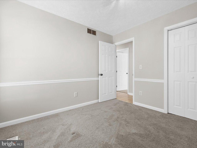 unfurnished bedroom with visible vents, carpet flooring, a textured ceiling, and baseboards