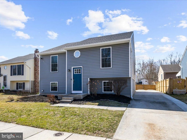 raised ranch with concrete driveway, a front yard, and fence