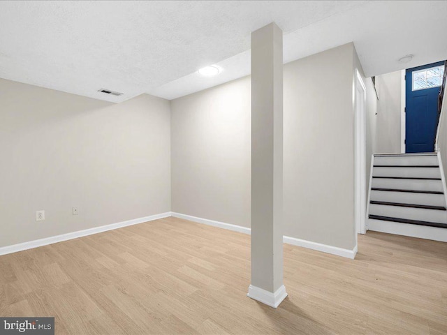 below grade area with light wood finished floors, visible vents, stairway, and baseboards