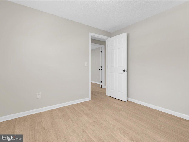 empty room featuring baseboards, light wood-type flooring, and a textured ceiling