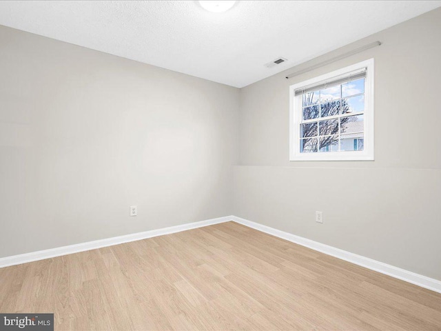 spare room featuring light wood finished floors, visible vents, a textured ceiling, and baseboards