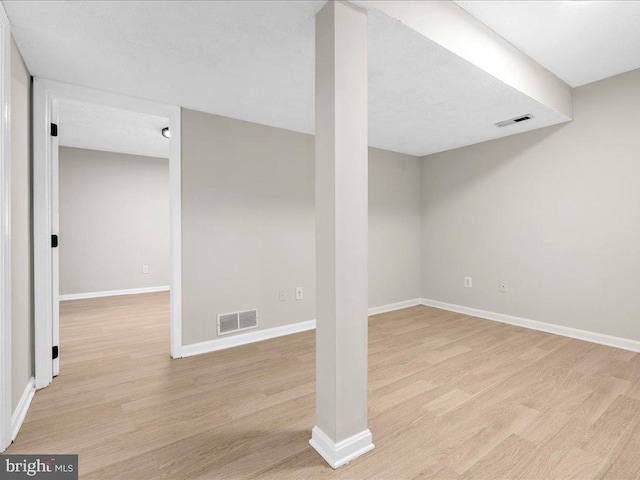 finished basement featuring visible vents, baseboards, and light wood finished floors