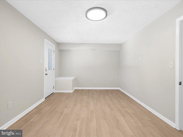 unfurnished room with light wood finished floors, a textured ceiling, and baseboards