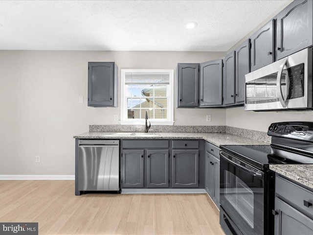 kitchen with a sink, light wood-type flooring, appliances with stainless steel finishes, and gray cabinetry