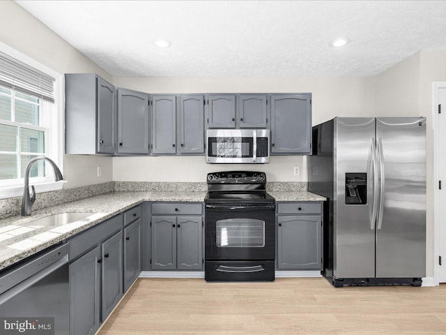 kitchen featuring a sink, appliances with stainless steel finishes, light wood-style flooring, and gray cabinets