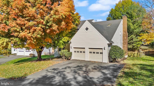 view of property exterior with aphalt driveway, a lawn, a garage, and a chimney