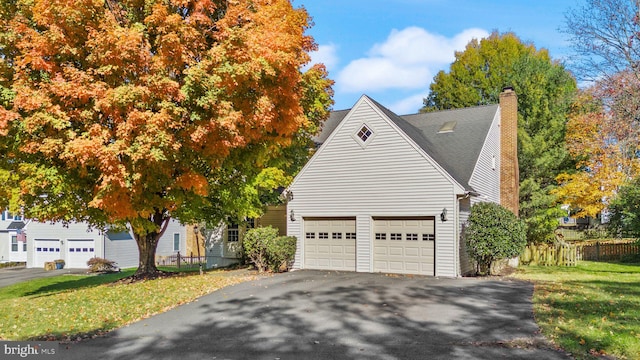 view of side of home featuring a lawn, driveway, fence, roof with shingles, and a chimney