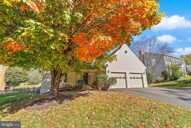 view of property hidden behind natural elements with aphalt driveway, fence, and a front lawn