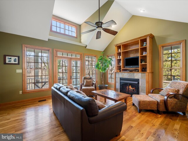 living area with a tile fireplace, french doors, high vaulted ceiling, and light wood-type flooring