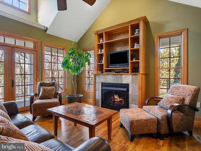 living area with light wood-type flooring, high vaulted ceiling, a ceiling fan, french doors, and a tile fireplace