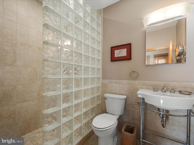 bathroom with a wainscoted wall, toilet, a sink, tile walls, and walk in shower