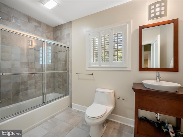 bathroom featuring toilet, vanity, baseboards, and shower / bath combination with glass door